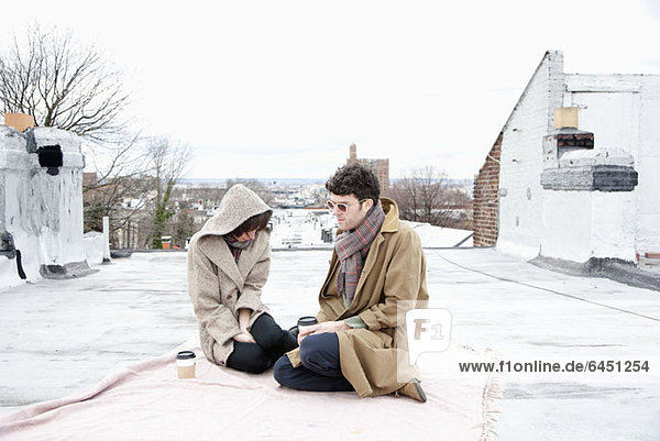 A young couple ignoring each other while sitting on a roof in winter