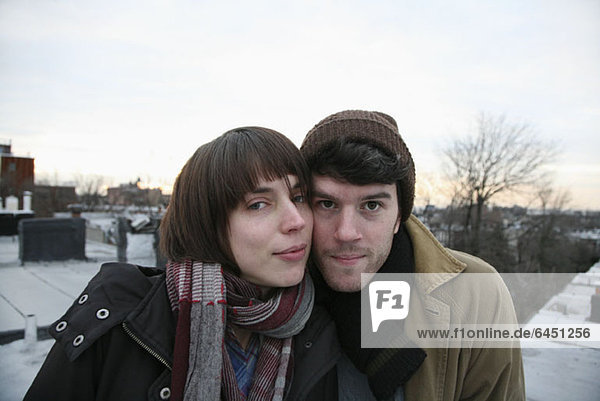 A young couple standing side by side on a roof in winter  Brooklyn  New York