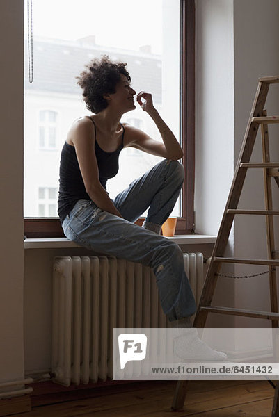 Eine Frau  die auf einem Fensterbrett sitzt und ihren Fuß auf einer Leiter ruht