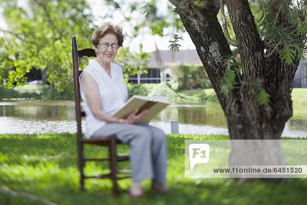 Eine ältere Frau liest am Fluss.