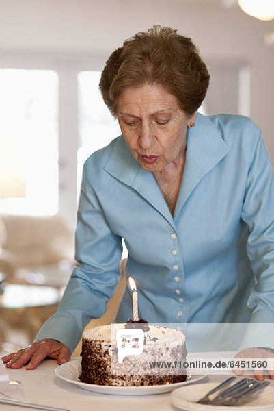 Eine ältere Frau  die eine Kerze auf einem Kuchen ausbläst.