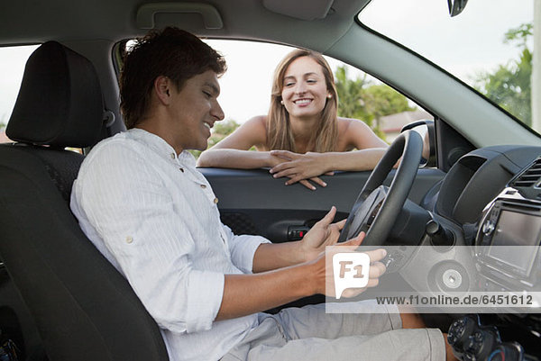 A woman leaning in car window smiling at boyfriend in the driver's seat
