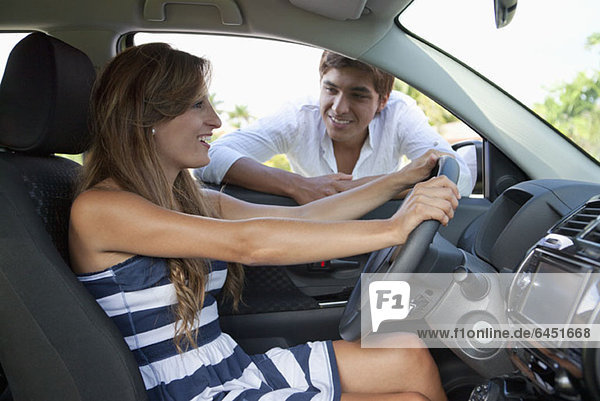 A man leaning in car window smiling at girlfriend in the driver's seat