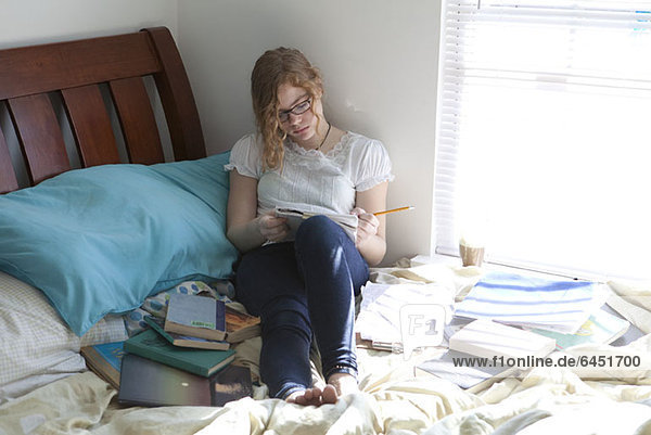 Beschäftigtes Mädchen mit Studienbüchern auf dem Bett