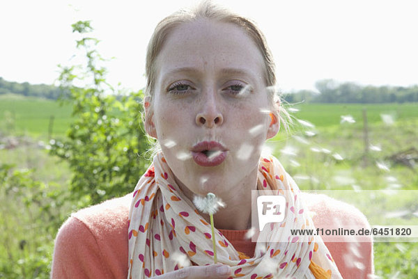 A woman blowing on a dandelion  close-up