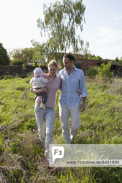 A man and a woman holding a baby walking in back of their country house
