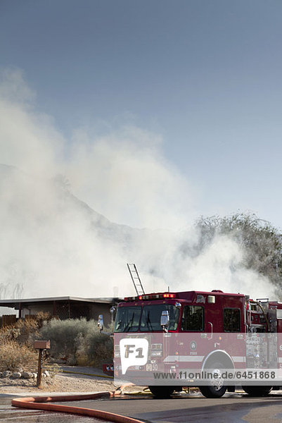 Ein Feuerwehrauto neben einem brennenden Haus in einem Vorort