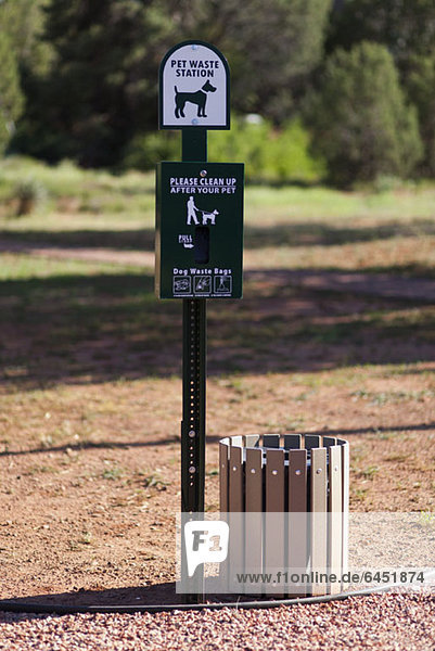 A sign and bin for pet waste in a park