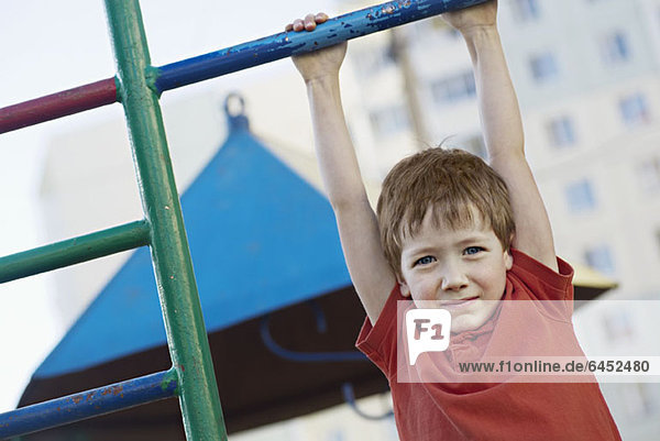 Ein Junge  der an einer Spielplatzbar hängt.