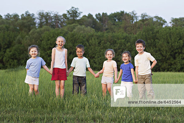 Kinder halten sich an den Händen und stehen auf einem Feld.