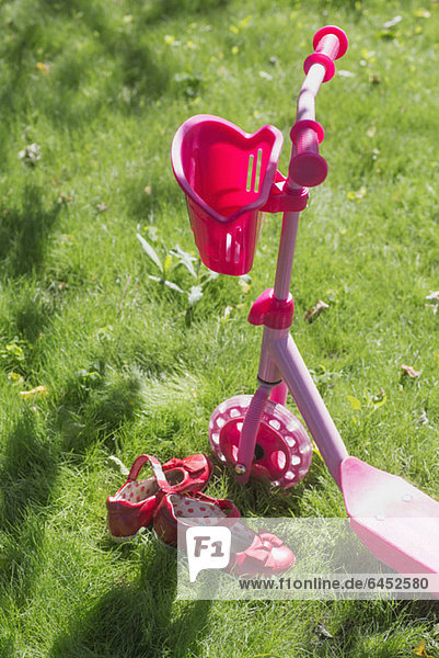Ein rosa Schiebescooter und rosa Schuhe eines Kindes auf Gras