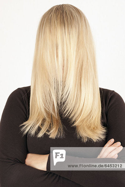 Eine Frau  die mit ihrem langen  blonden Haar nach vorne gekämmt steht und ihr Gesicht bedeckt.