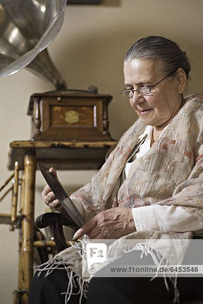 Eine ältere Frau  die intensiv auf eine Schallplatte schaut  Grammophon im Hintergrund