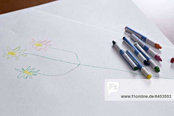 Buntstifte  die auf einer Kinderzeichnung eines Stängels mit Blumen liegen