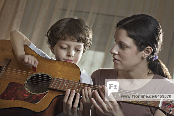 A mother helping her young son with playing an acoustic guitar