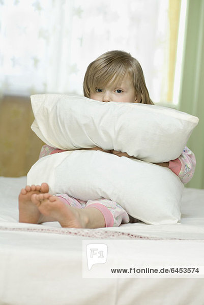 Ein kleines Mädchen  das traurig aussieht  während es ein Kissen drückt.