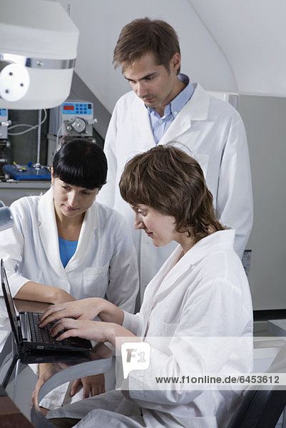 Zwei Labortechniker  die als dritter Techniker Notizen auf einem Laptop ansehen.