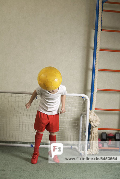 Ein kleiner Junge  der einen Fußballball von einem Tor weg springt.