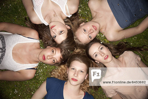 Five female friends lying in the grass in a circle looking sensually at the camera