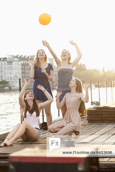 Four female friends tossing a ball around on a jetty next to Spree River  Berlin  Germany