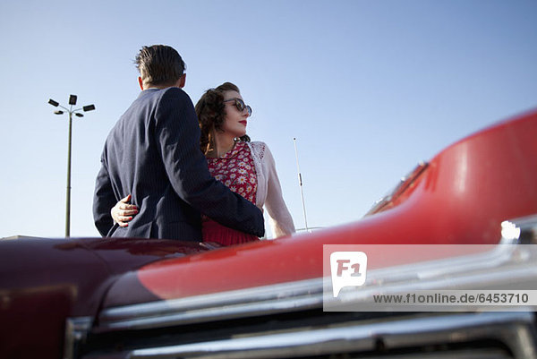 A cool  rockabilly couple with arms around each other by a vintage car