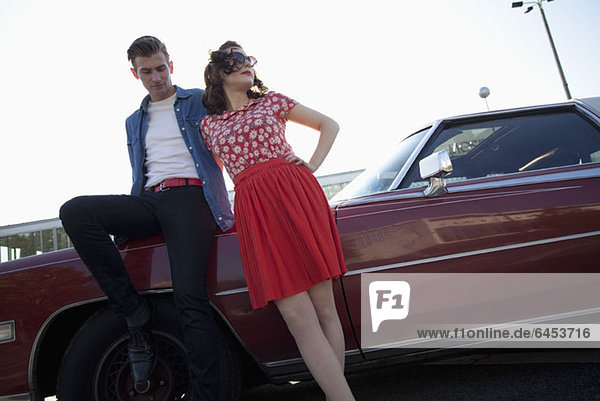 A cool  rockabilly couple leaning against a vintage car