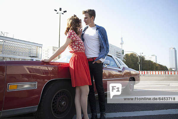 A flirtatious rockabilly couple standing next to a vintage car  Berlin  Germany