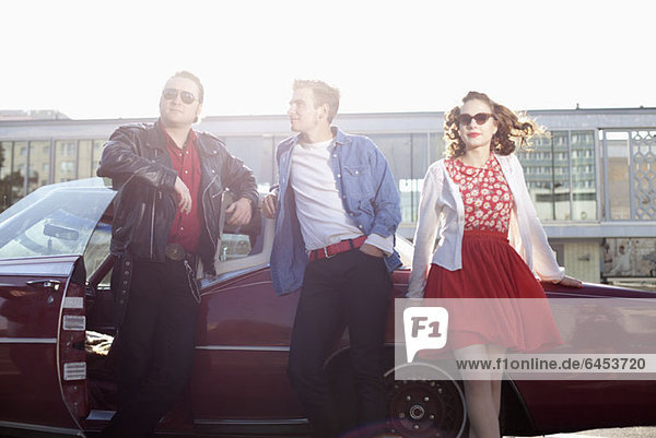 Three rockabilly friends leaning against a vintage car