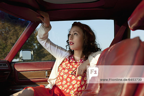 A pretty rockabilly woman pulling a sun visor down in a vintage car