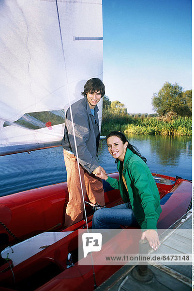 1216671 outdoor day summer couple young man woman girl boy brunette dark haired 20-25 stand sit water lake blouse blouses green grey sailing boat red vacation holidays recreation hold hand hands help get out moor smile smiling vertical