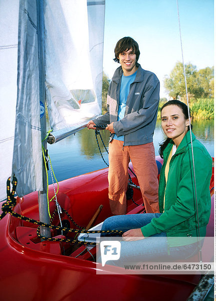 1216673 outdoor day summer couple young man woman girl boy brunette dark haired 20-25 stand sit water lake blouse blouses green grey sailing boat red vacation holidays recreation hold hawser cordage set sail smile smiling close up vertical