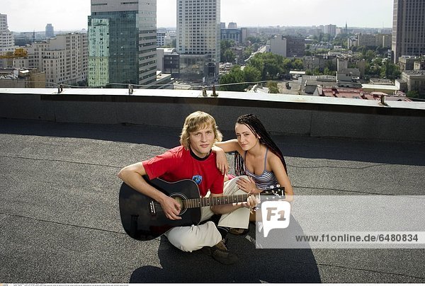 1229492 outdor roof city day summer people couple young man woman fair haired boy 20-25 girl woman brunette long hair pigtail pigtails sit cross leg legs smile smiling hold play guitar instrument musical horizontal