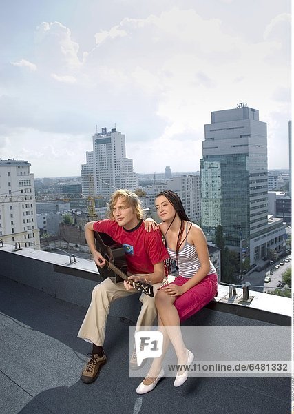 1229496 outdor roof city day summer people couple young man woman fair haired boy 20-25 girl woman brunette long hair pigtail pigtails sit smile smiling hold play guitar instrument musical embrace vertical