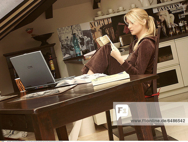 1221067 indoor flat room young woman blonde long hair ponytail 25-30 sit chair table brown blouse laptop notebook personal computer work internet communication book books hold read profile horizontal