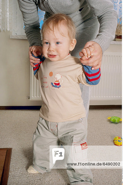 1234387 indoor flat room people baby boy 0-5 fair haired green trousers beige blouse stand go woman fragment hold hand hands mother son assist help close up vertical