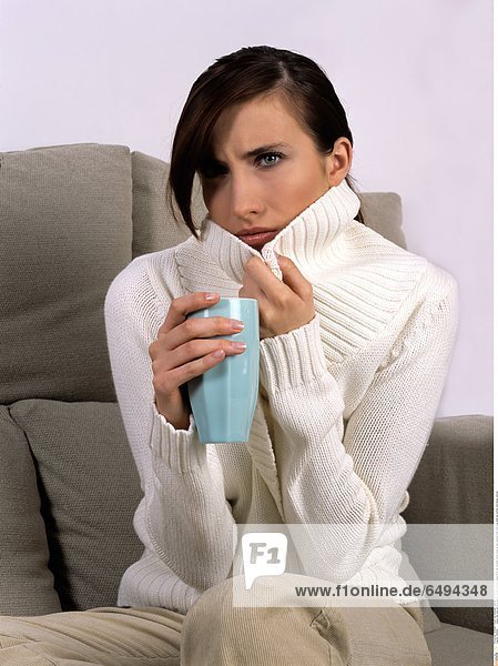 1239362 indoor flat room sit sofa people woman brunette young 20-25 girl sweater white close up sad sadness think hold mug drink tea coffee cold illness vertical