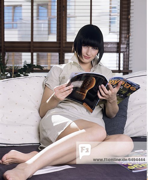 1239139 indoor flat room people woman young girl 20-25 brunette fringe rest relax hobby read newspaper newspapers vertical smile smiling foot feet barefoot