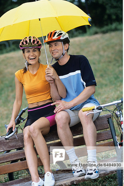 1239296 outdoor day summer vacation people woman young 20-25 girl smile smiling blouse orange shorts black park relax rest sport helmet sit bench man couple dark haired helmets hold yellow umbrella fun play vertical blouses blue bike bikes ride 25-30