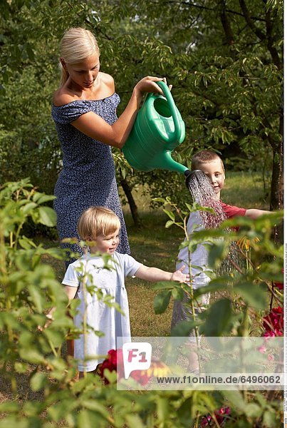 1243662 outdoor day summer garden people child boy 5-10 fair haired tree trees rest relax smile smiling blouse red white woman young 25-30 blonde long haired dress blue watering can cans water stand vertical flower flowers children girl 0-5 blondes