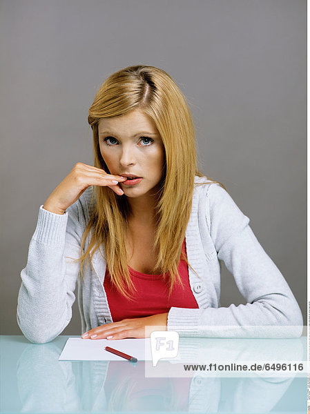 1243462 indoor studio people woman young 25-30 blonde long haired close up study sad sadness table paper pencil write sweater white blouse red vertical finger nail bite