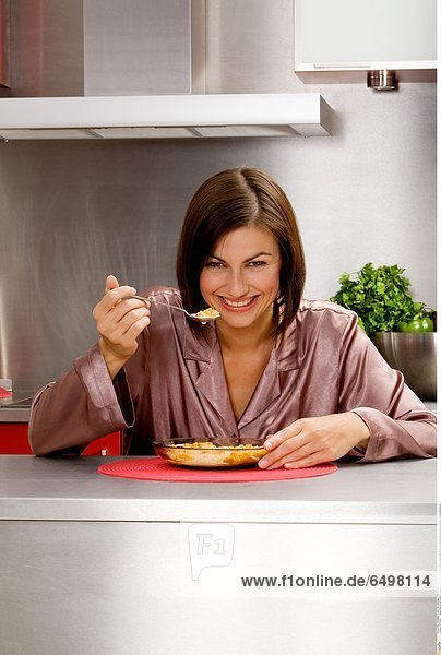 1247204 indoor flat kitchen people woman young 25-30 brunette close up hand hold robe smile smiling vertical eat breakfast cereal plate spoon