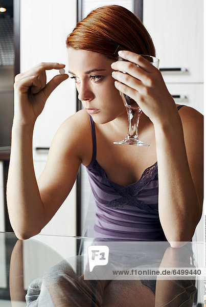 1249201 indoor flat people woman young girl 20-25 blonde medicine close up kitchen blouse violet vitamin drink glass water hand hold sad sadness think vertical