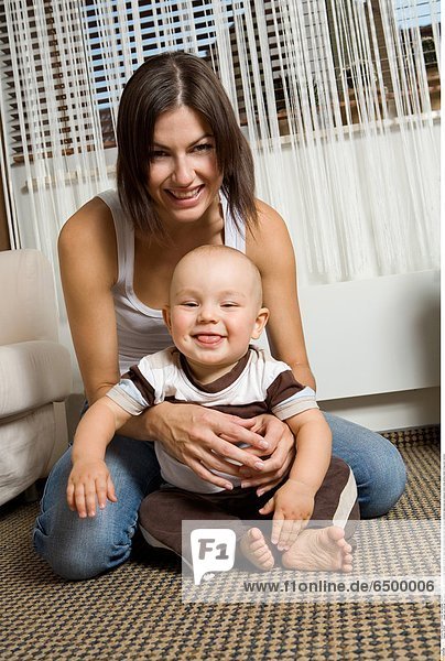 1252287 people two child girl boy woman mother motherhood son douther 0-5 25-30 years adult brunette bare foot feet tongue emotions happyness joy pleasure mime smile smiling indoor living-room vertical