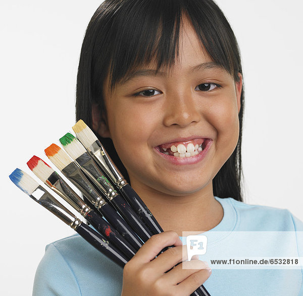Asian girl holding paintbrushes with different colors on bristles