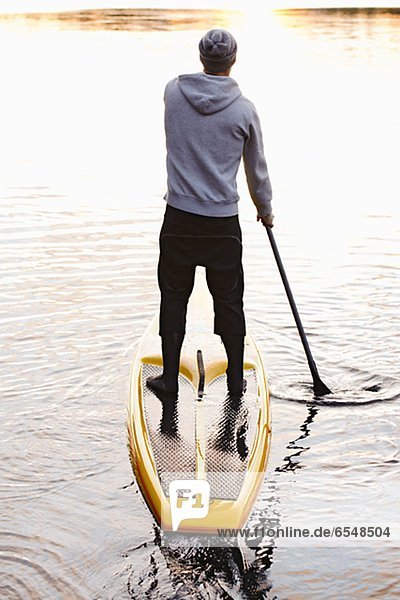 Man rowing paddle board in water  rear view