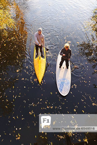 Two people rowing paddle boards in autumn trees  elevated view