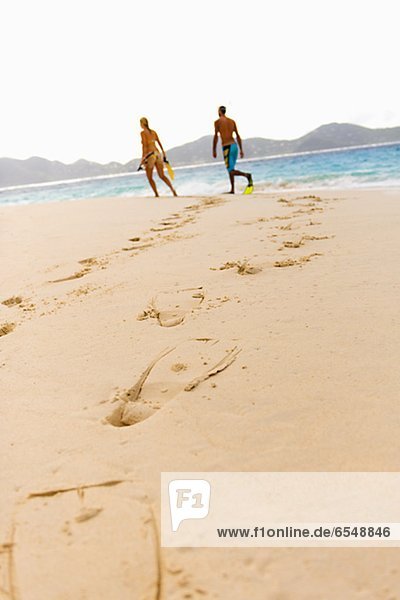 Diving flipper prints on sand,  mid adult couple in background