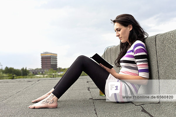 Junge Frau sitzt auf dem Dach und liest Buch