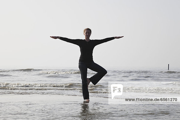 Belgium  Young woman standing in tree pose at North Sea
