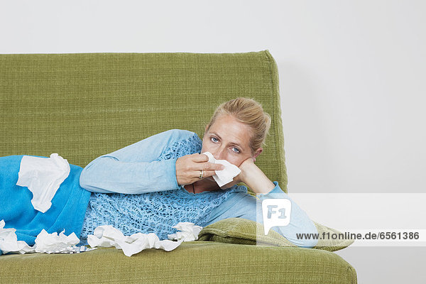 Mature woman blowing nose while lying on sofa